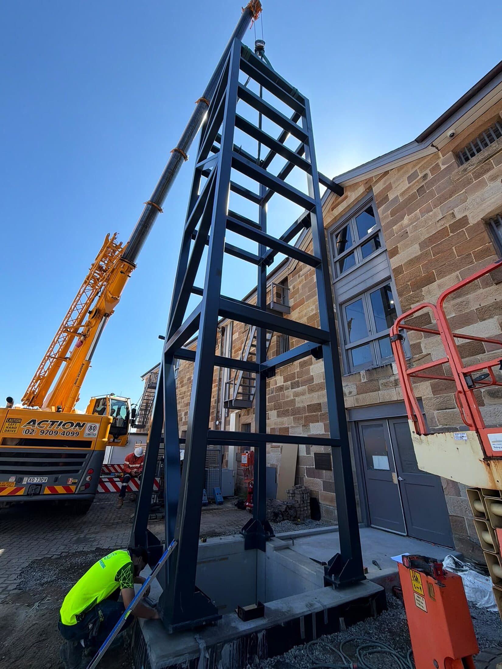 Steel lift shaft frame standing upright as it is lowered into its pit